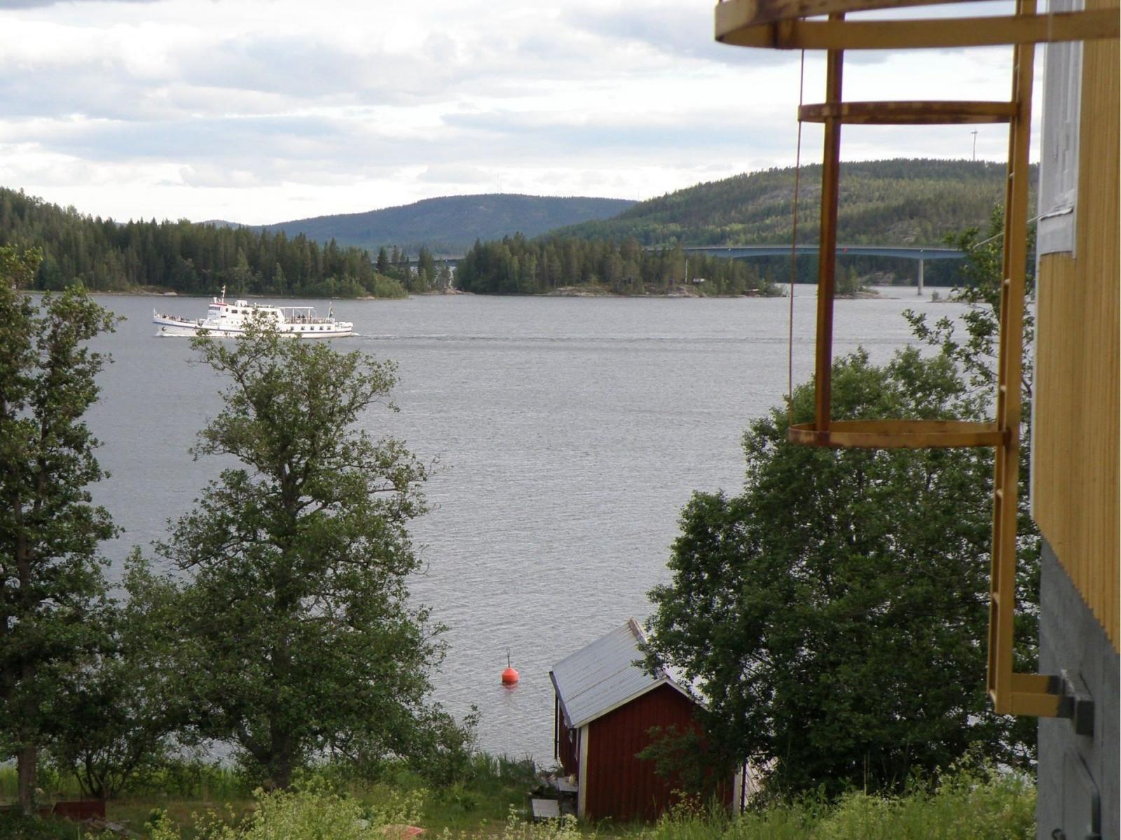 Till höger på bilden syns kortsidan av huvudbyggnaden. Vid vattnet ligger sjöboden där det också finns logi. På fjärden passerar Ådalen III